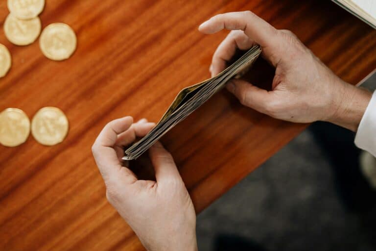 A cropped image of a man's hand stacking paper bills while coins scatter on the table in the concept of saving money when moving to Uxbridge.