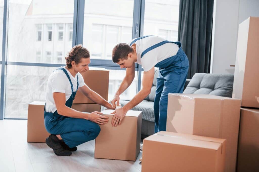 House movers busy with sealing cardboards on the moving day in the concept of 'How to Choose the Best Home Removals Company'.